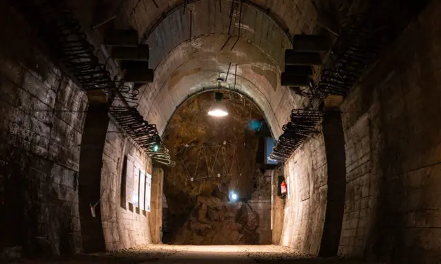 Wnętrze tunelu w Górach Sowich. Betonowe ściany, łukowe sklepienie i skalna grota z instalacją świetlną.