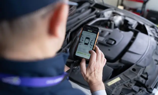 Mechanik sprawdza na telefonie raport z pomiaru lakieru i szczelin, szukając potencjalnych **kody błędów** w samochodzie.