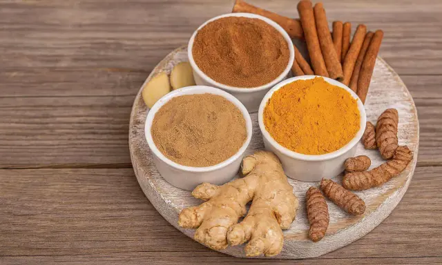 Poudre de curcuma, gingembre frais et bâtons de cannelle sur une planche en bois. Idéal pour un thé réconfortant au curcuma et miel.