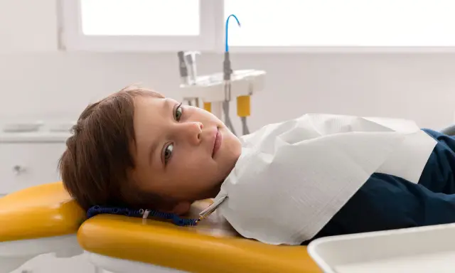 Chłopiec leży na żółtym fotelu dentystycznym, przygotowany do leczenia zębów pod narkozą.