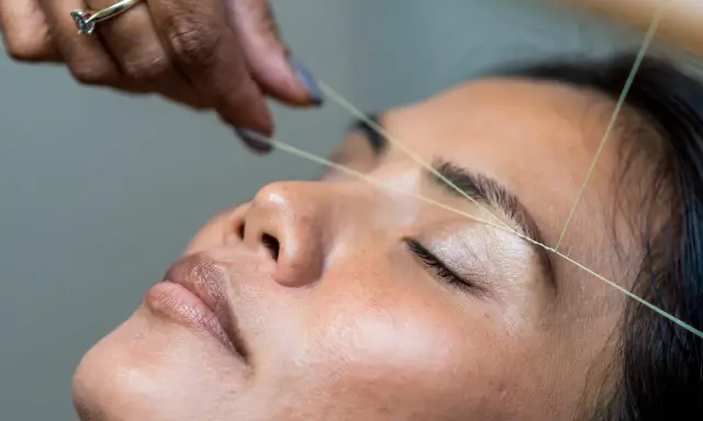 Une main utilise un fil pour épiler ses sourcils.