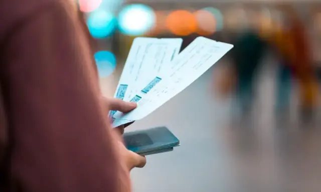 Dłoń trzymająca kilka biletów lotniczych i paszport.