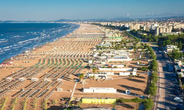 La riviera romagnola dove andare: una distesa infinita di ombrelloni e lettini sulla sabbia dorata, con il mare azzurro e la città sullo sfondo.