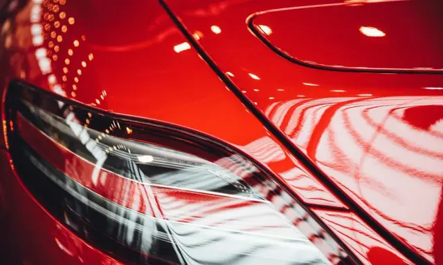 Błyszczący, czerwony lakier samochodu, odbijający światła. Widać fragment lampy. To praca detailera, który doprowadził auto do perfekcji.