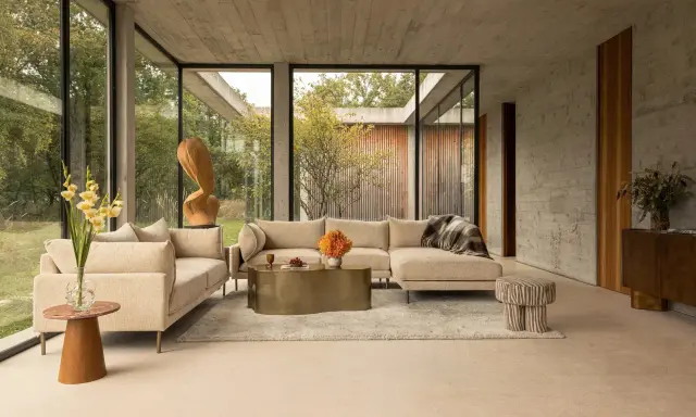 Un salon moderne avec un canapé beige, une table basse dorée et des touches de couleur orange et verte. Une question se pose : quelle couleur assortir avec le beige pour un intérieur chaleureux ?