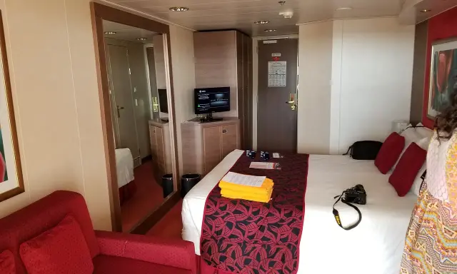 Cabina MSC Musica con letto, divano rosso, specchio e TV. Perfetta per una vacanza in crociera.