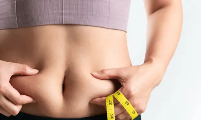 Frau kneift Bauchfett, Maßband zeigt Umfang. Tipps für 10 Hausmittel gegen Bauchfett.