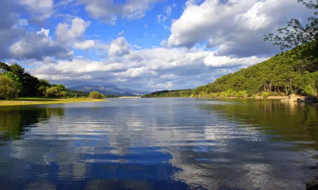 El embalse La Jarosa, con su agua serena reflejando el cielo nublado y rodeado de verdes colinas, invita a la calma.