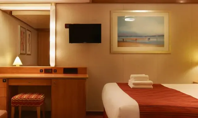 Accogliente cabina interna crociera con letto, specchio, scrivania e TV.