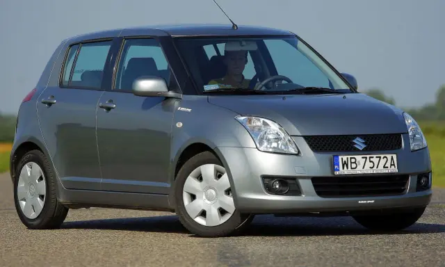 Szary Suzuki Swift 2007 z kierowcą za kierownicą, zaparkowany na drodze.