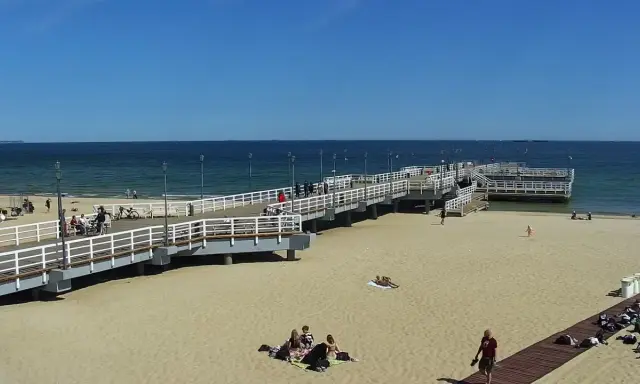 Słoneczny dzień na gdańskiej plaży Brzeźno. Ludzie spacerują po molo, odpoczywają na piasku, ciesząc się widokiem morza.