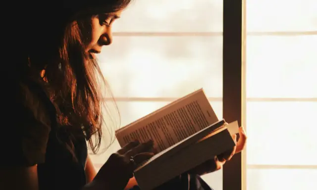 Ragazza immersa nella lettura, illuminata dalla luce dorata del tramonto, sfoglia pagine che potrebbero contenere i libri di Emmanuel Carrère.