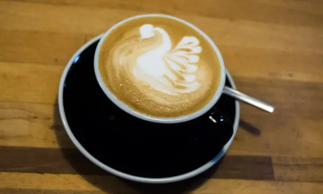Cappuccino mit Milch-Schwan-Latte-Art auf schwarzer Untertasse. Perfekt für jeden Kaffeeliebhaber.