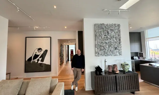 Guy Hepner stands in a modern apartment filled with art, including a large black and white drawing and a textured sculpture.