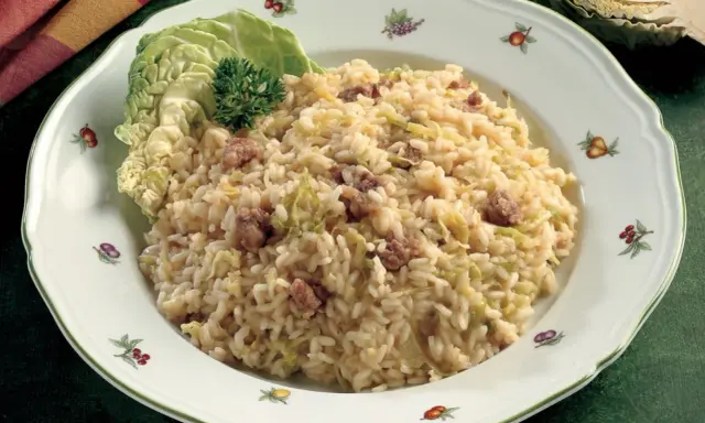 Un saporito risotto con verza e salsiccia, guarnito con una foglia di verza fresca e un ciuffo di prezzemolo.
