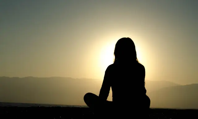 Silhuett av en person som mediterar vid solnedgången. Kanske är det en av nackdelar med meditation att man blir så fokuserad att man missar allt annat.