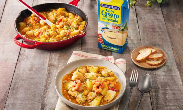 Rape a la marinera con patatas y gambas, servido en cazuela roja y plato. Al lado, caldo de pescado Gallina Blanca y pan tostado.