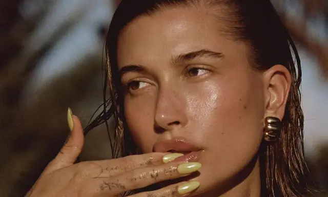 Mujer con brillos en la cara, uñas amarillas y tatuajes en la mano.
