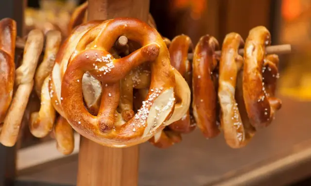 Des bretzels dorés, saupoudrés de gros sel, sont suspendus sur un support en bois. Ces spécialités lorraines invitent à la dégustation.