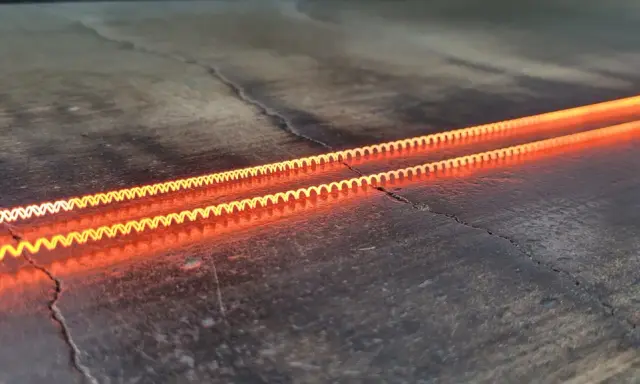 Dos espirales incandescentes, demostrando el efecto Joule en una caldera, brillan con un naranja intenso sobre una superficie oscura y agrietada.