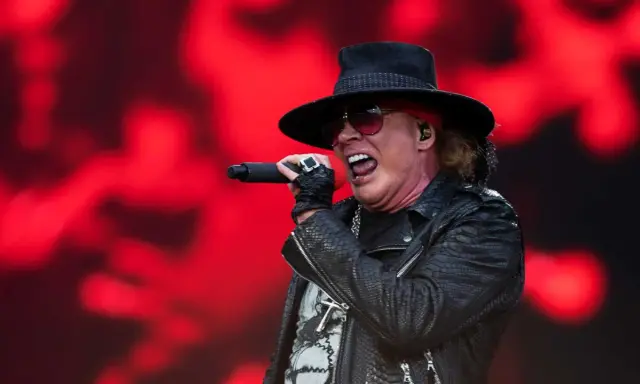 Axl Rose sjunger med en röd bakgrund. Trots rykten om axl rose sjukdom, levererar han en energisk show.