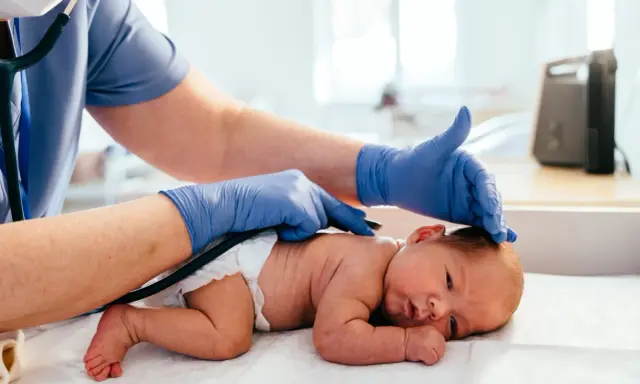 Medico controlla la schiena di un neonato, notando una piccola fossetta sacrale.