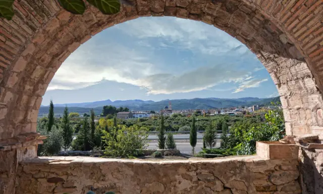Vista de un pueblo desde un arco de ladrillo. Un paisaje con montañas y vegetación, ideal para ver en altura.