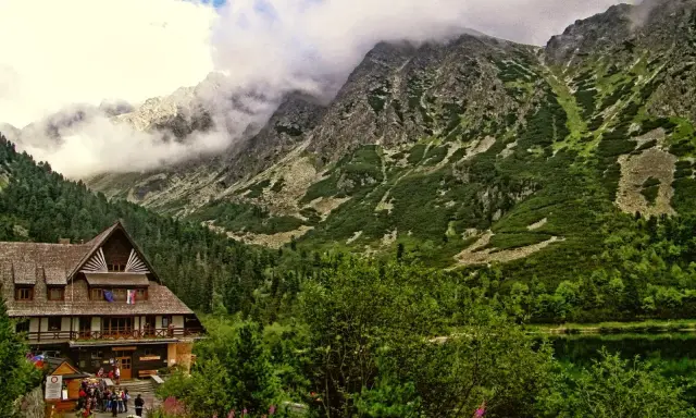 Drewniany budynek schroniska tatry w otoczeniu zielonych zboczy i skalistych gór, nad spokojnym jeziorem.