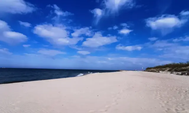 Pusta plaża z wydmami i latarnią morską, idealna na weekendowe odkrywanie magicznych miejsc nad Bałtykiem.