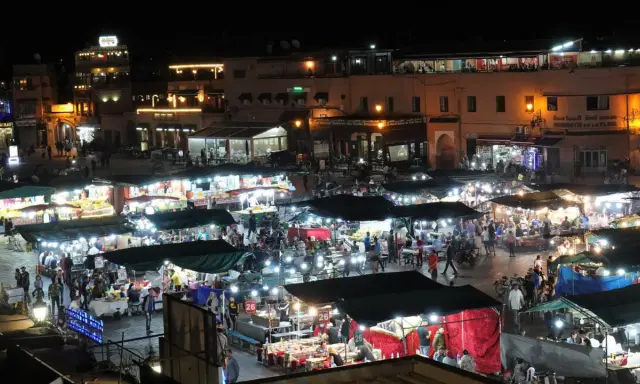 Belebter Marktplatz in Marokko bei Nacht. Viele Stände mit Lichtern und Menschen, die einkaufen und essen. Wann ist Ramadan in Marokko?