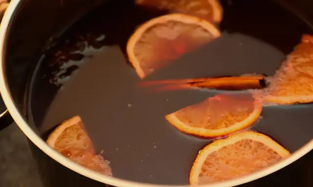 Une marmite remplie d'un liquide sombre, avec des tranches d'orange, un bâton de cannelle et de l'anis étoilé. Parfait pour une recette punch simple et réconfortante.