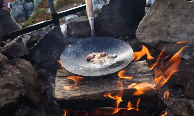 Stekt fläsk i stekpanna över öppen eld, en del av ett recept kolbullar. Elden sprakar och röken stiger.