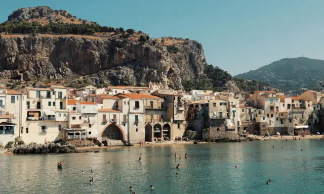 Un incantevole borgo da visitare in Sicilia, con case color pastello affacciate sul mare cristallino e una maestosa roccia a fare da sfondo.