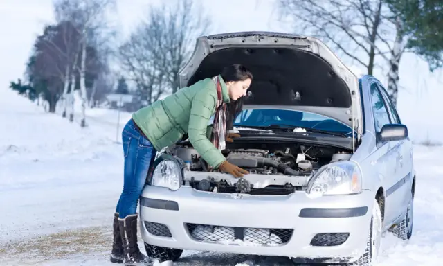 Kobieta w zimowej kurtce sprawdza silnik samochodu na śniegu. Zastanawia się, w jakiej temperaturze zamarza diesel, by uniknąć problemów.