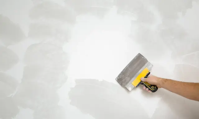 Mano con espátula aplicando masilla para alisar la pared, un paso clave en cómo quitar el gotele con espátula.