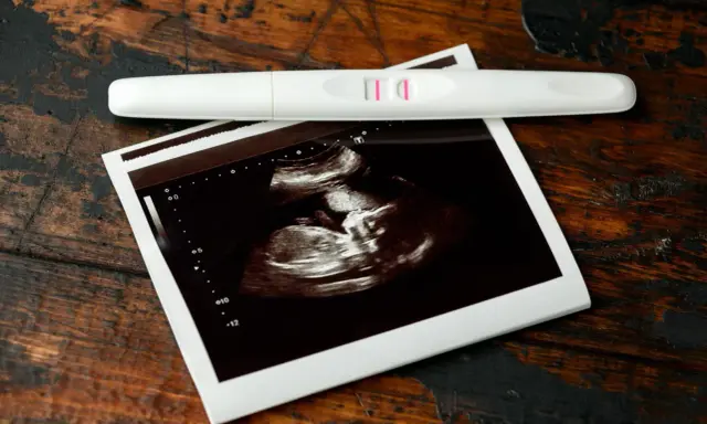 USG 7 tydzień ciąży pokazuje zarodek. Obok leży pozytywny test ciążowy.