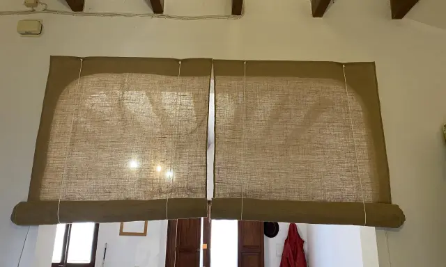 Dos estores enrollables caseros de tela de yute cubren una ventana y una puerta.