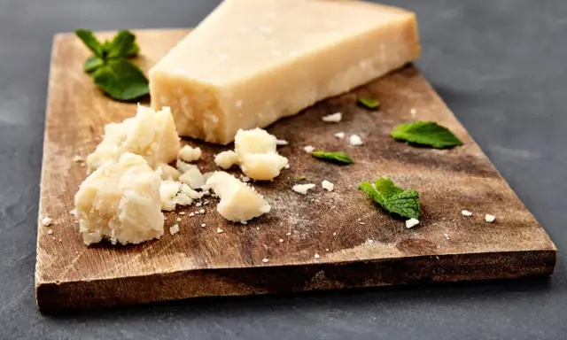 Ein Stück und zerbrochene Stücke von ist parmigiano parmesan liegen auf einem Holzbrett, garniert mit Minzblättern.