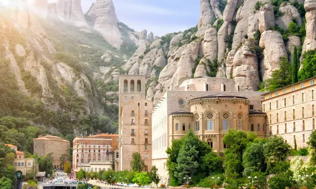 Klasztor Montserrat wznosi się wśród skalistych szczytów, z budynkami o architekturze przypominającej czcionkę Montserrat.