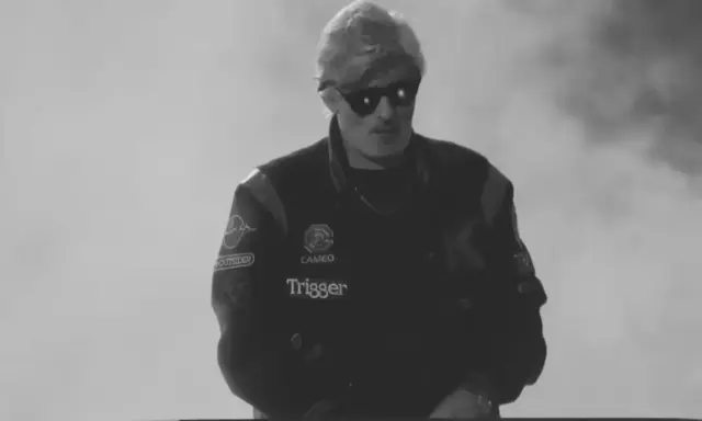 Młody artysta w okularach przeciwsłonecznych, w kurtce z naszywkami, gotowy do występu. Jego styl to czysty ras hip-hop.