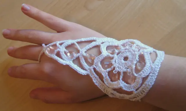 Ett vackert virkat armband i vitt med pärlor, som pryder en hand.