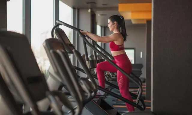Frau macht ein Stairmaster Workout im Fitnessstudio. Sie trägt ein rotes Sportoutfit und trainiert intensiv.