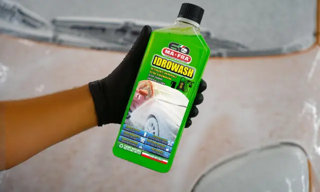 Mano con guanto nero tiene bottiglia di Idrowash, un detergente schiumoso verde brillante per auto.