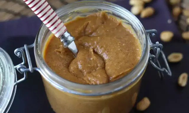 Un pot de praliné cacahuète onctueux, prêt à être dégusté. Quelques cacahuètes parsèment le plan de travail.