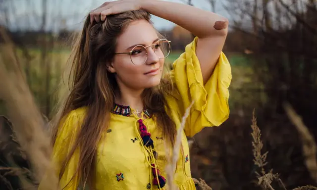 Portret dziewczyny w okularach i żółtej sukience, wśród traw. Różne rodzaje portretów w fotografii mogą uchwycić taką naturalną, swobodną chwilę.