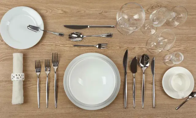Une table dressée avec un **caractère élégant** : assiettes blanches, couverts en argent, verres à pied et une serviette décorée.