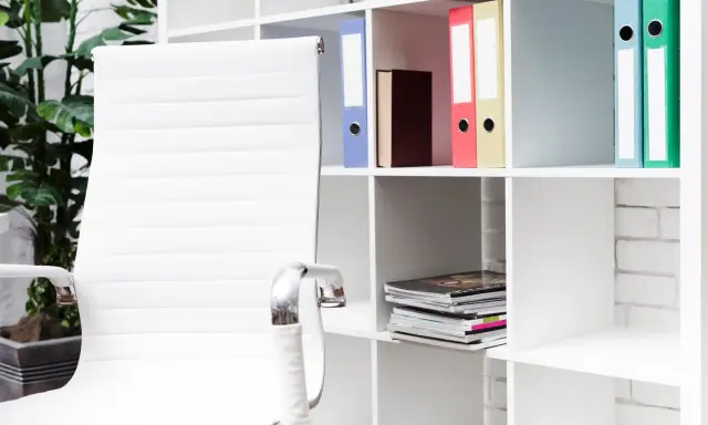 Scrivania ordinata con sedia bianca e scaffali pieni di raccoglitori colorati, perfetti per chi cerca idee su come organizzare i documenti di casa.