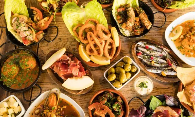 Vielfältige Tapas ideen: Tintenfischringe, Sardinen, Garnelen, Fleischbällchen, Schinken mit Melone, Oliven und mehr auf Holztisch.