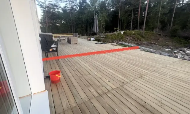 Nybyggd altan med en röd markering som visar var ett vindskydd ska byggas. Trädgårdsmöbler och en parasoll finns på plats.