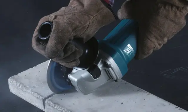 Manos enguantadas usan una radial para cortar hormigón. La radial es una herramienta eléctrica versátil para cortar y desbastar.